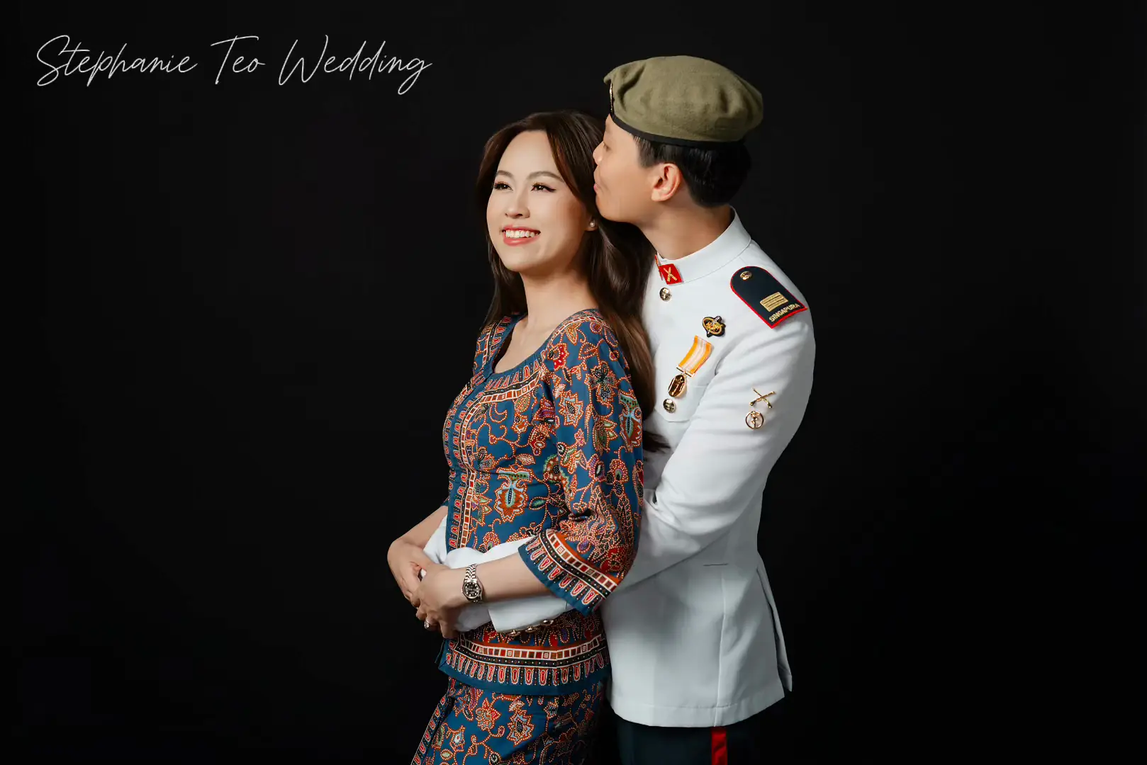 Bride in a beaded kebaya and groom in ceremonial white uniform, studio portrait on black